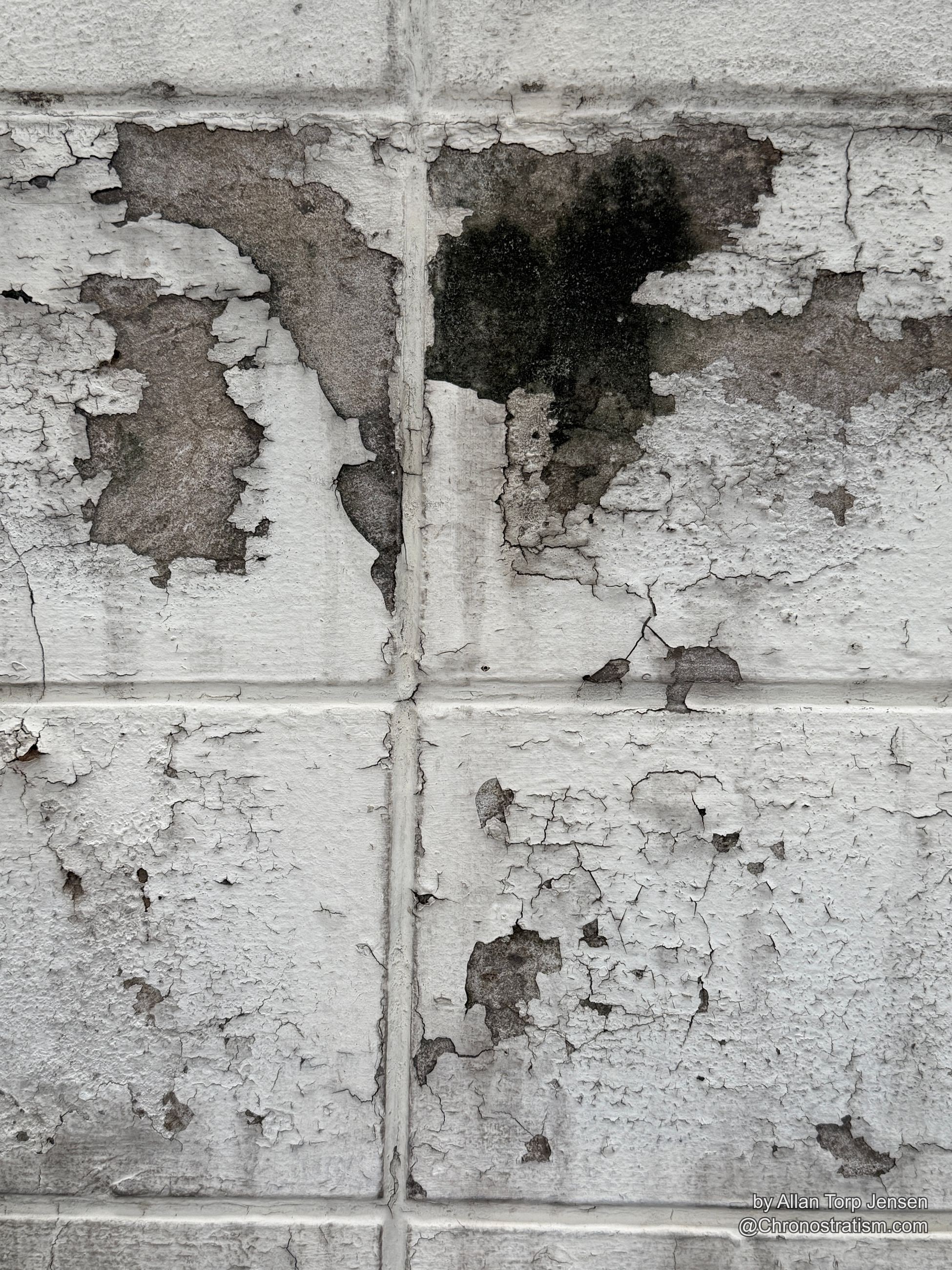 A stark black soot-like stain interrupts the same tiled wall's peeling white paint, sitting beside more typical tan patches of exposed substrate.