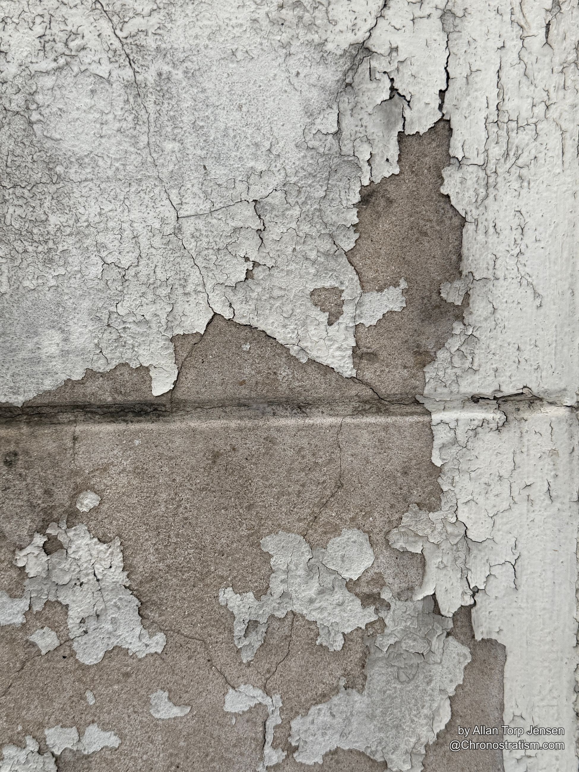 Peeling paint gives way along a vertical seam in the tiled wall, tan substrate showing through in broad uneven patches.