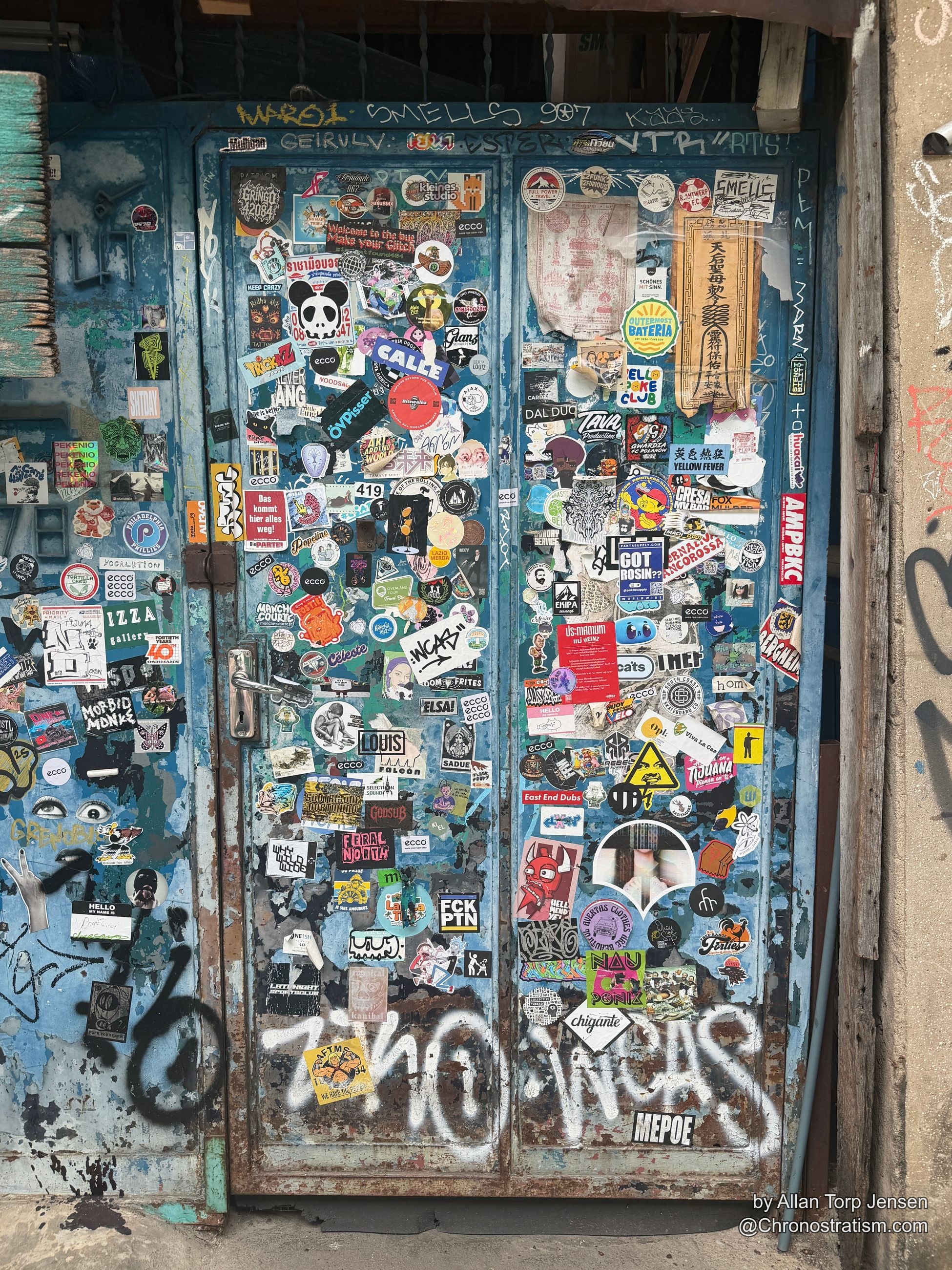 A blue-painted door armoured in dozens of overlapping stickers and spray tags.