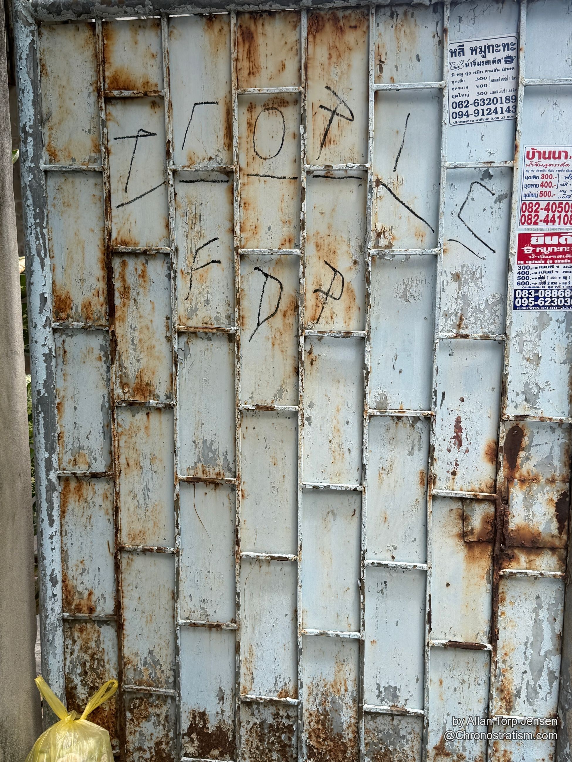 A brick-patterned metal cladding panel rusts heavily beneath faded signage stickers and marker scrawl.