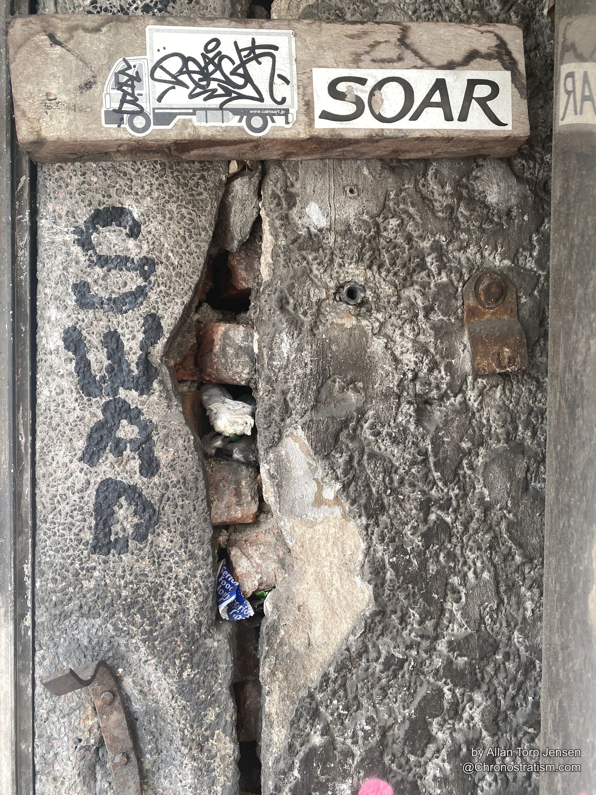 Corroded reinforcement bar and tie wire exposed at a broken concrete corner.