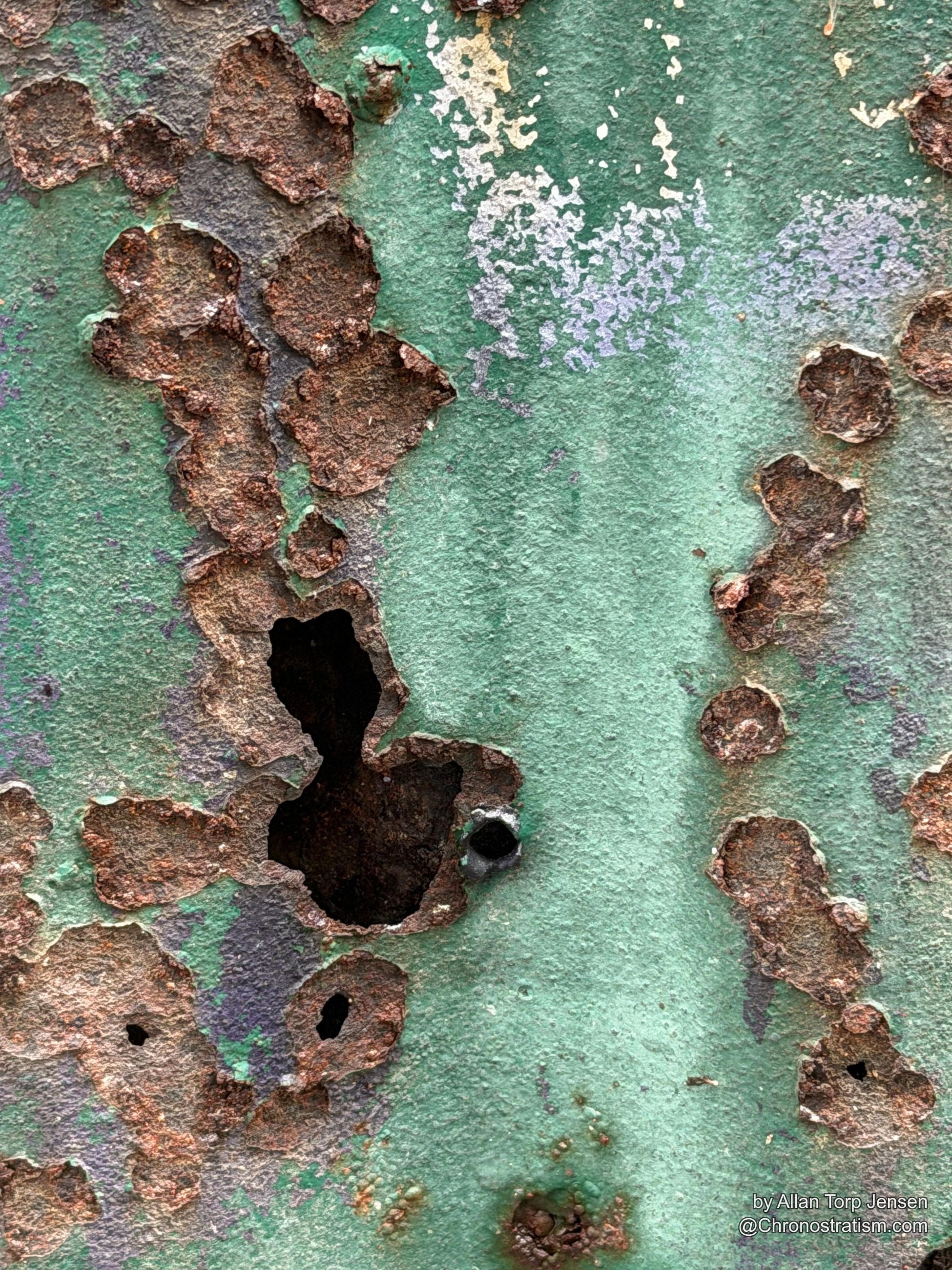Cream paint flakes away from rusted metal in a wide torn patch, cracks spreading through the coating.