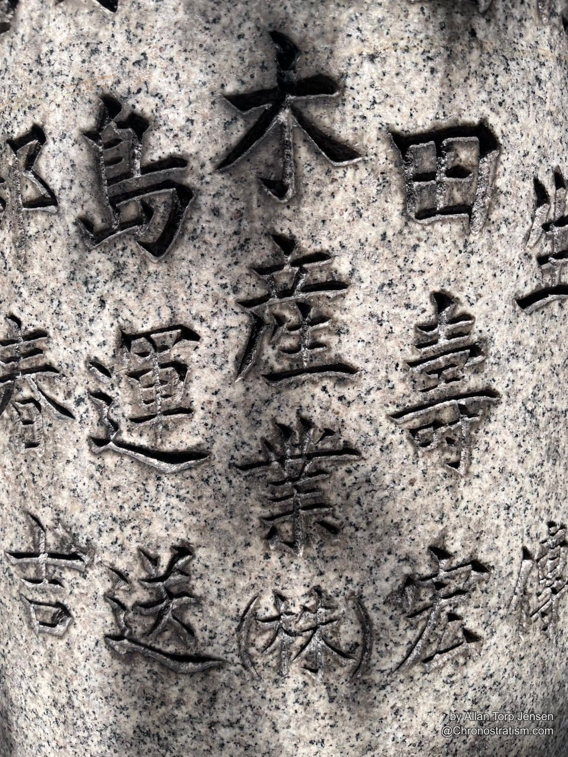 Deep-carved kanji characters fill a speckled granite memorial stone.