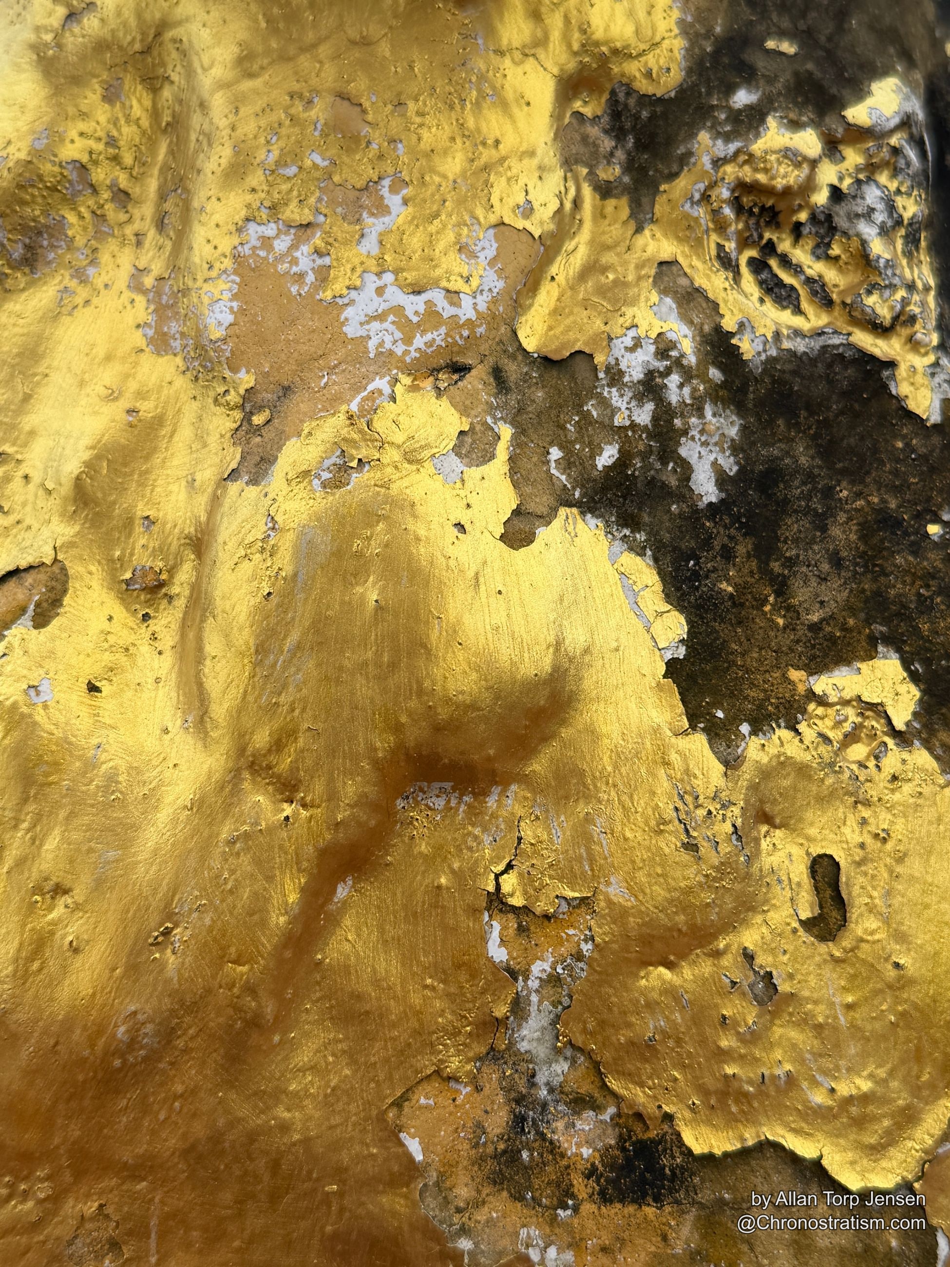 Dense black soot eats into cracked gold leaf across the statue’s surface.
