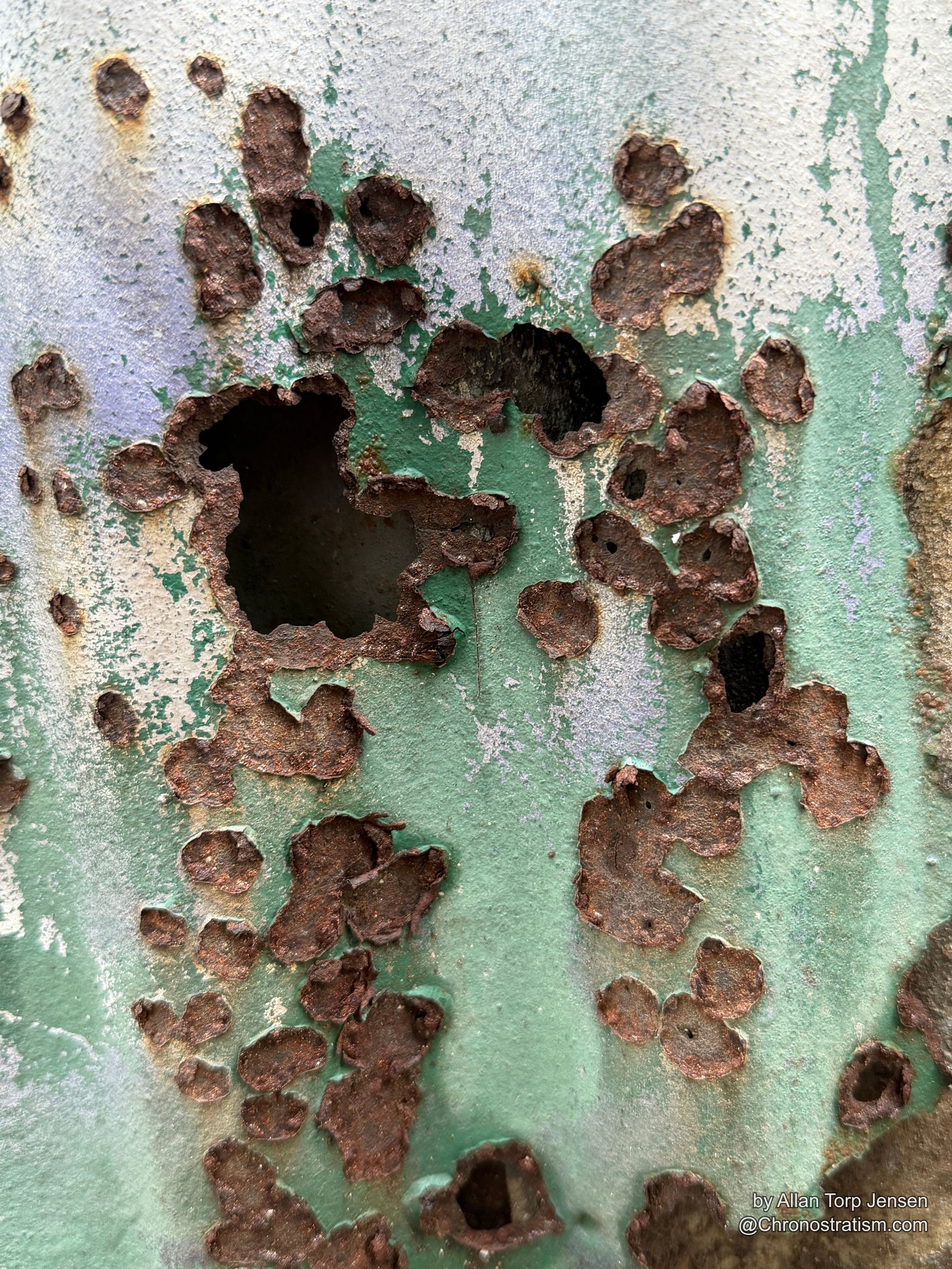 Dense clusters of rust perforate a pale green painted metal sheet.