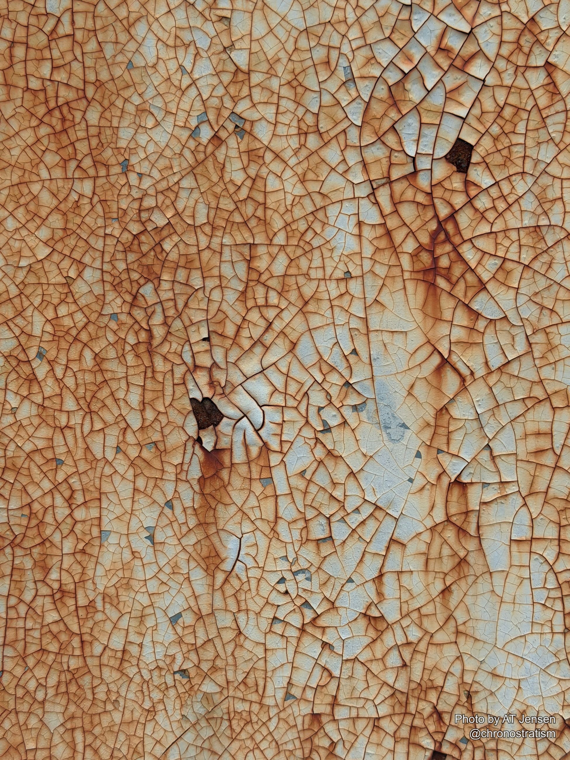 Dense micro-cracking laces a cream-painted surface, rust seeping through scattered dark fissures.