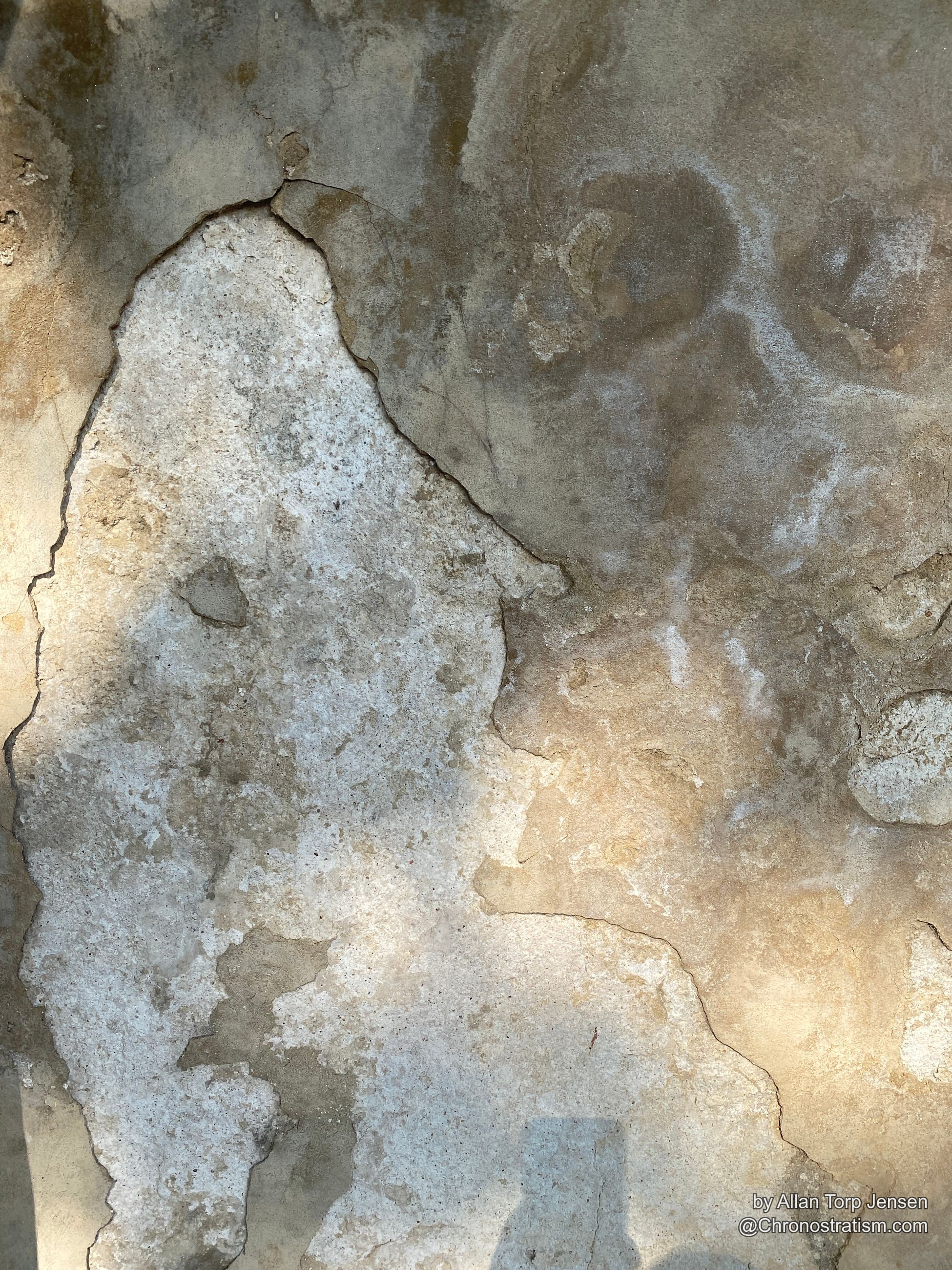 A diagonal hairline crack through mould-stained tan plaster render.