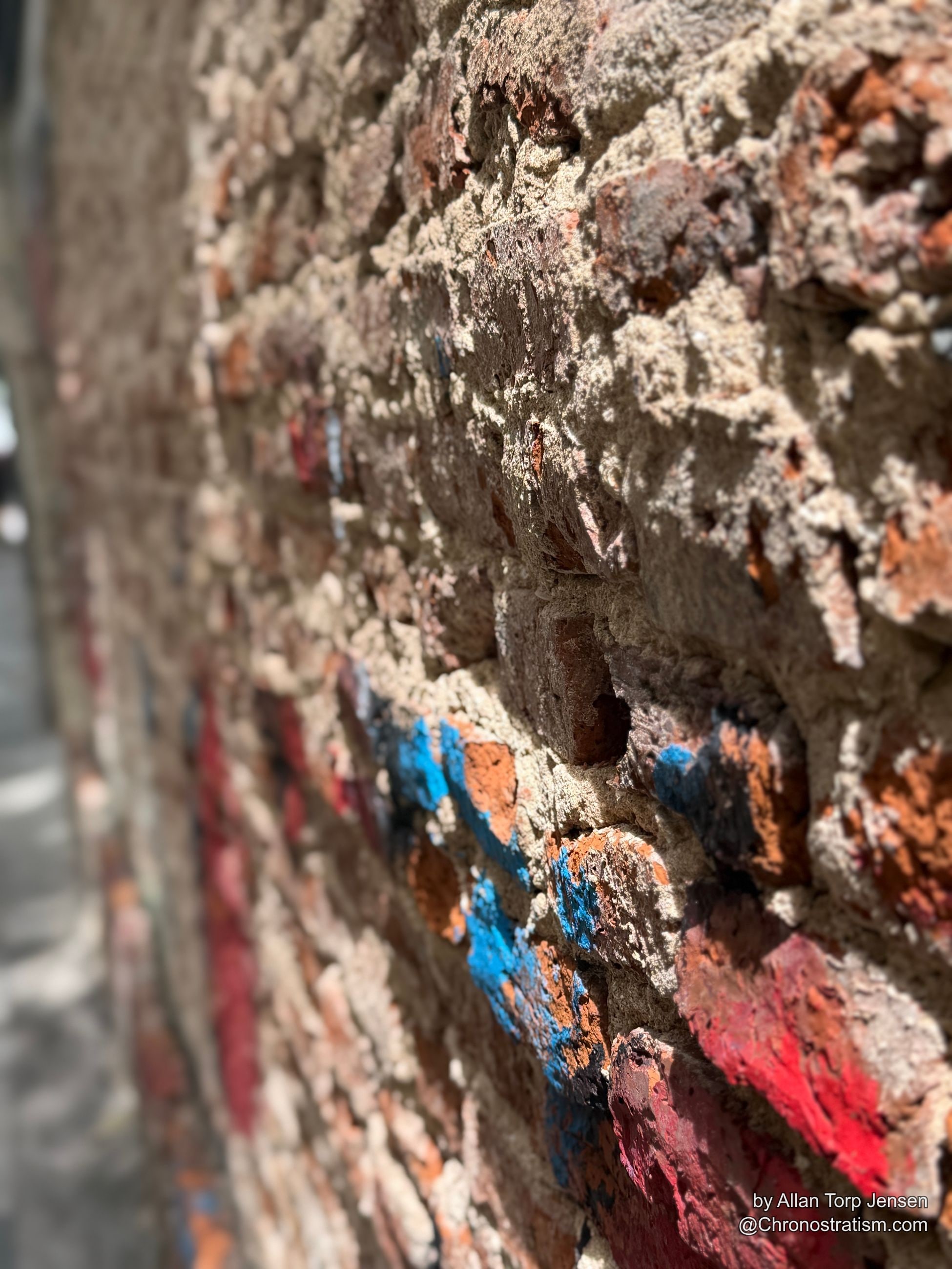 Faint red and blue paint traces linger on aged, patched brickwork.