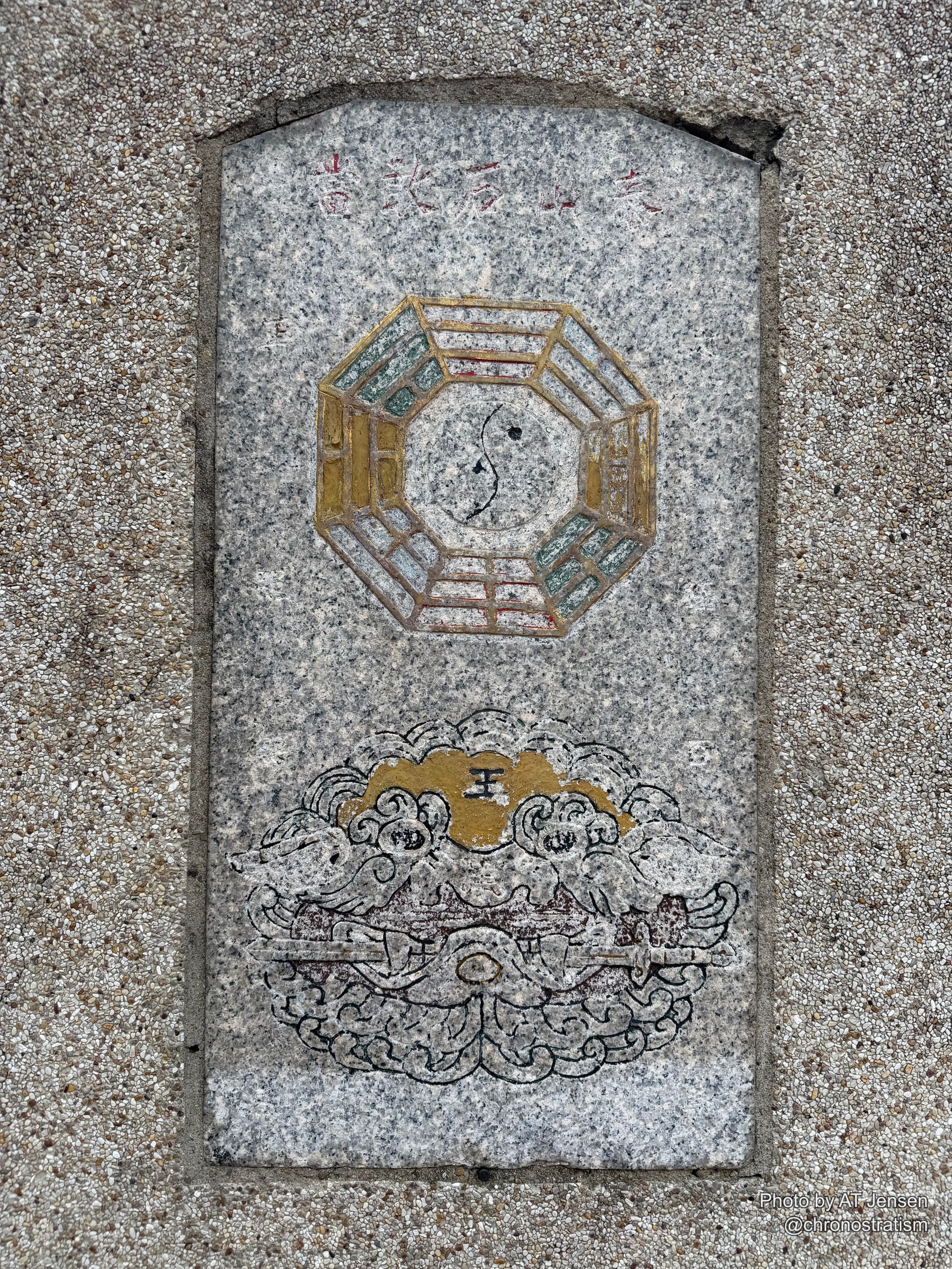 A gilded bagua mirror and carved guardian figure are inlaid into a granite pavement slab.