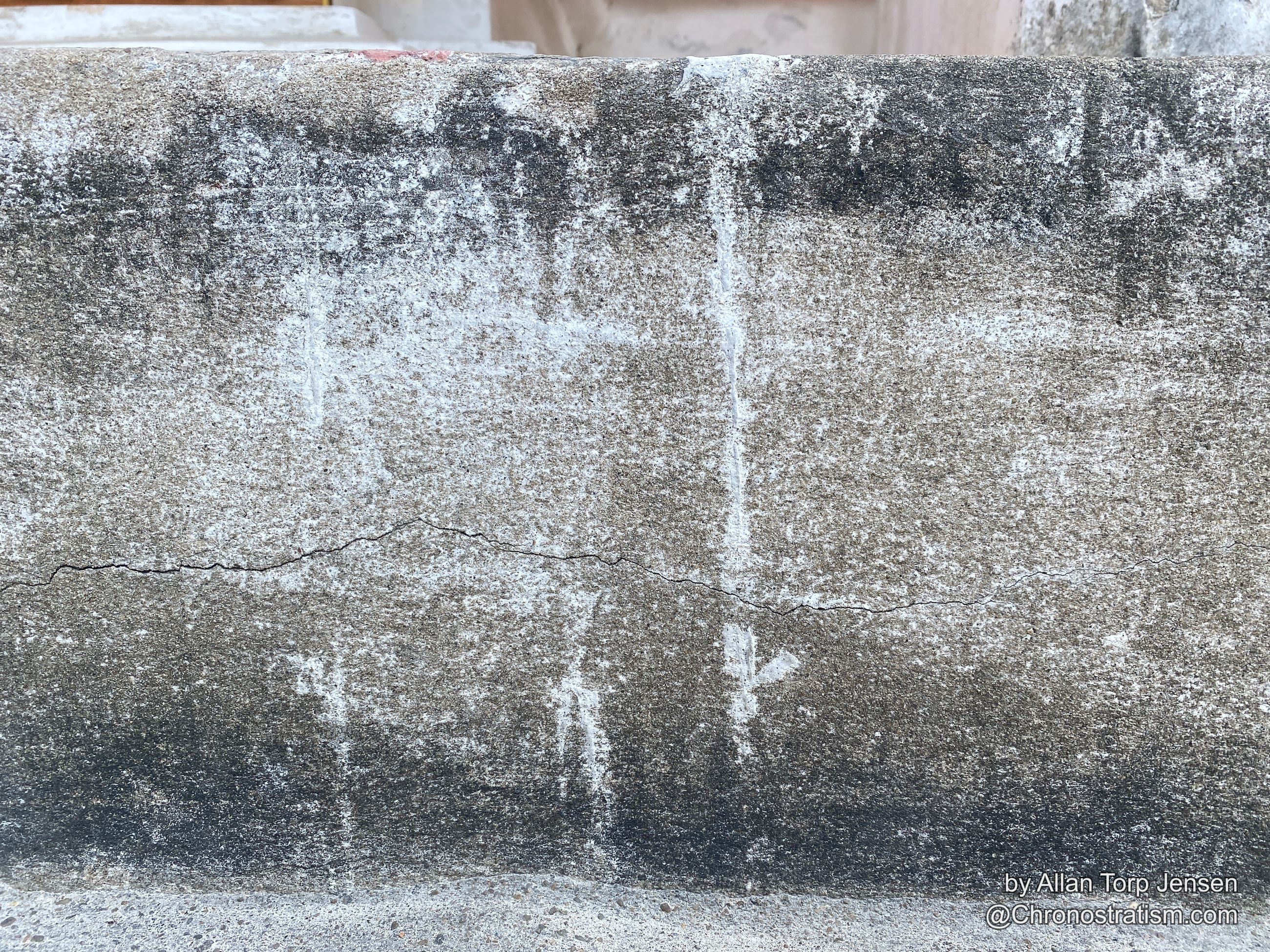 A hairline crack runs through weathered stone with white salt efflorescence blooming across it.