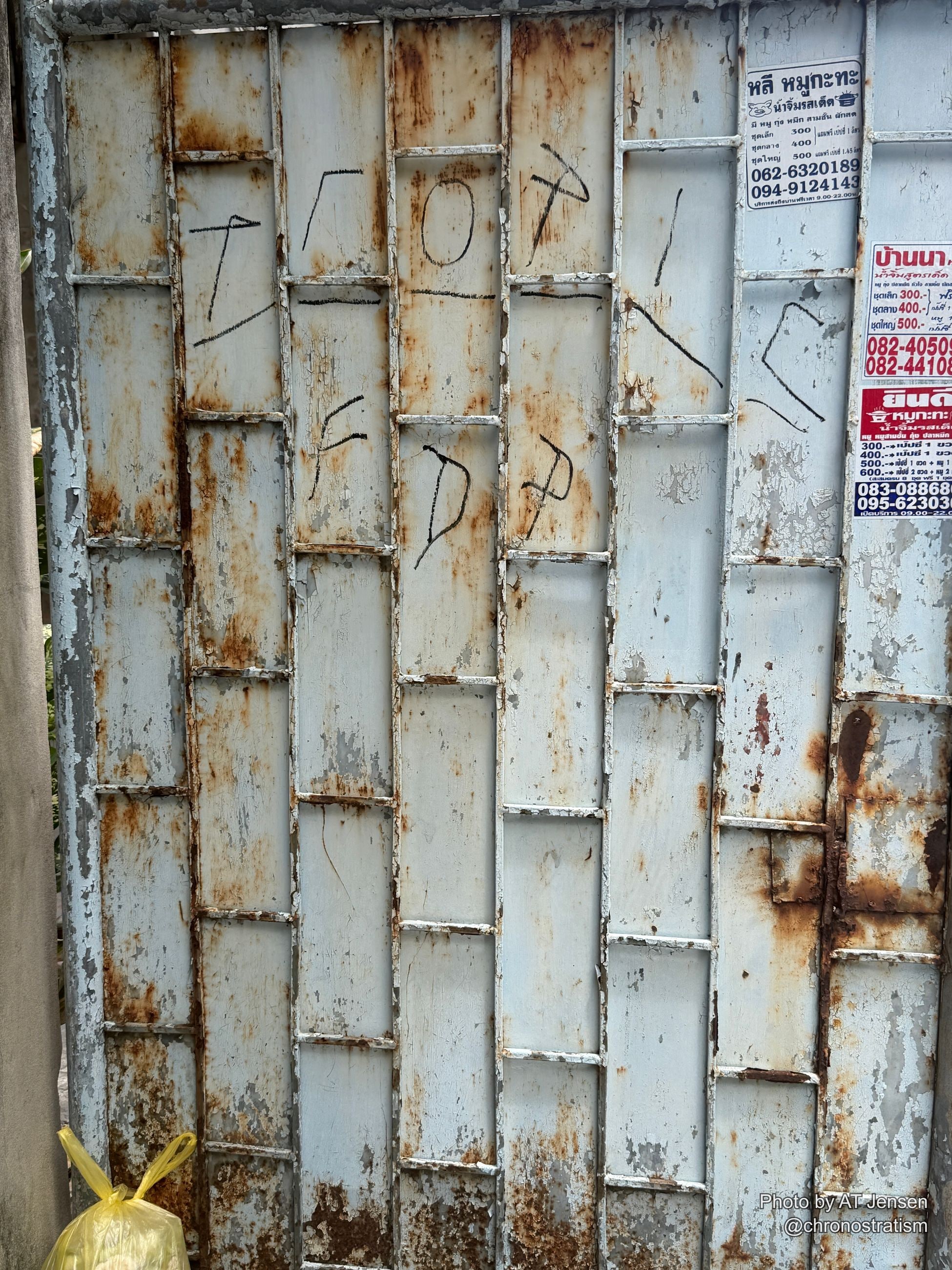 Hand-scrawled chalk doodles and business phone-number stickers cover a rusty corrugated wall.
