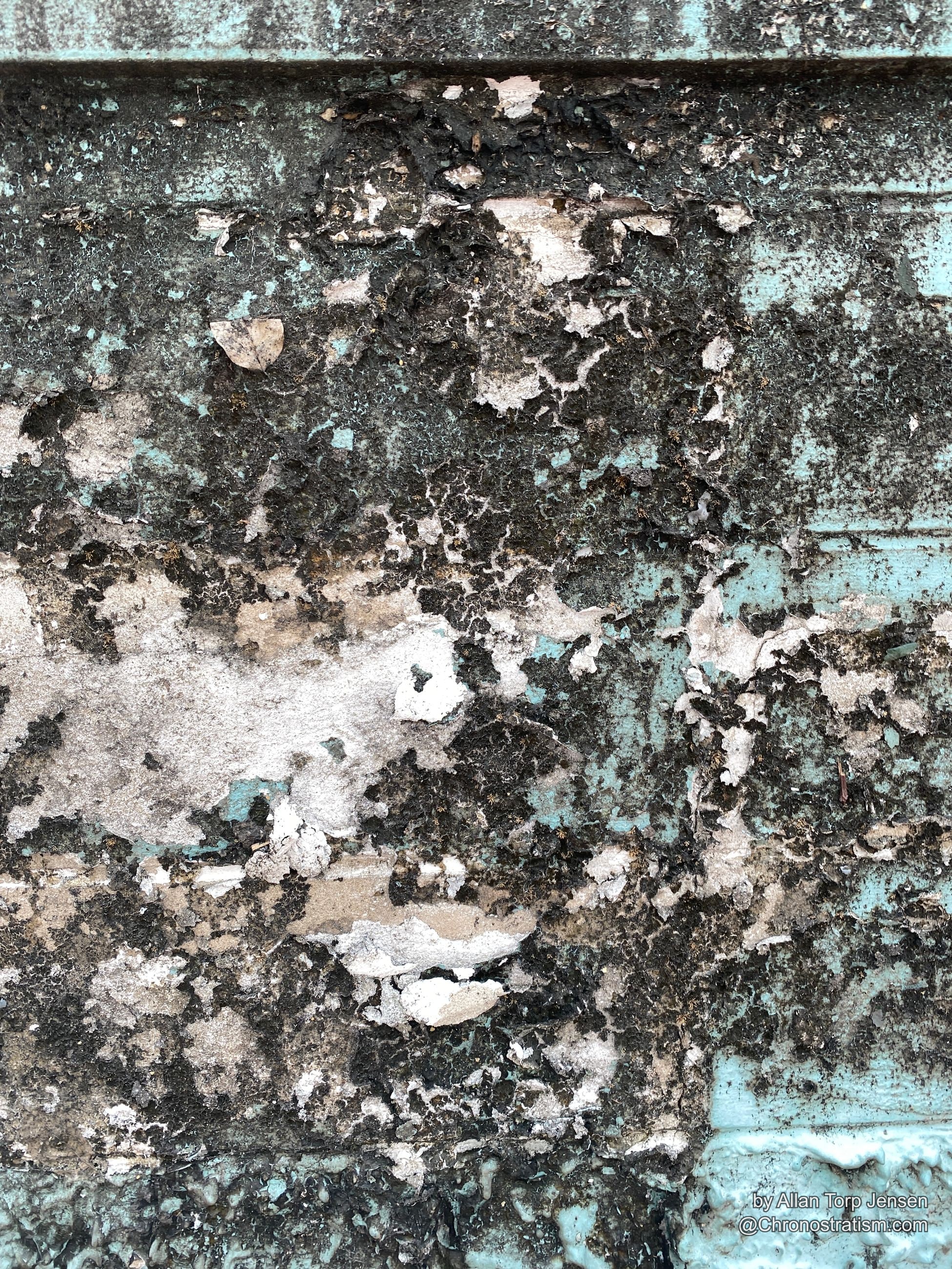 Heavy black crust breaking through peeling teal paint on wood siding.