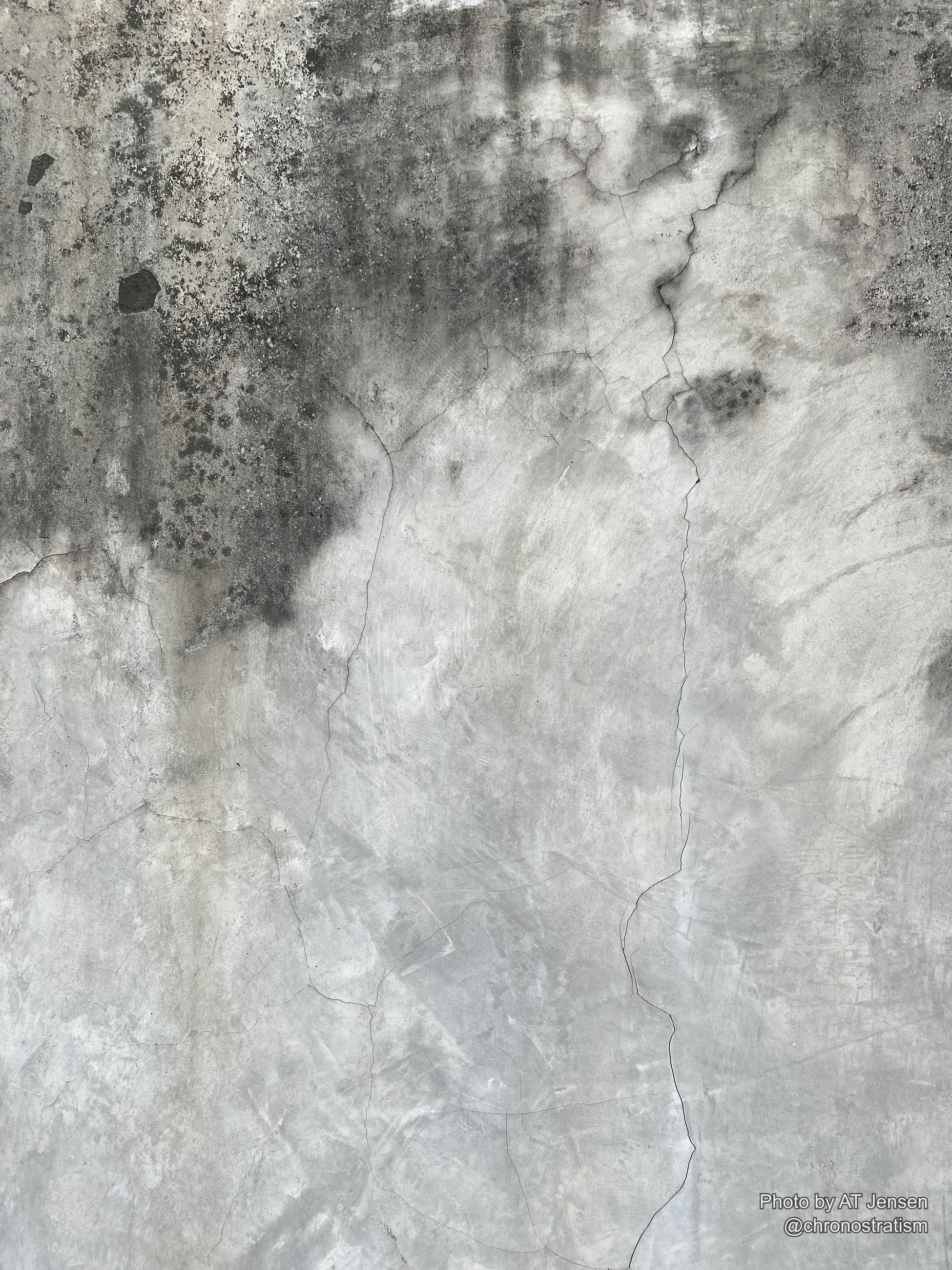 A network of thin cracks spreads across a grey concrete wall stained with soot.