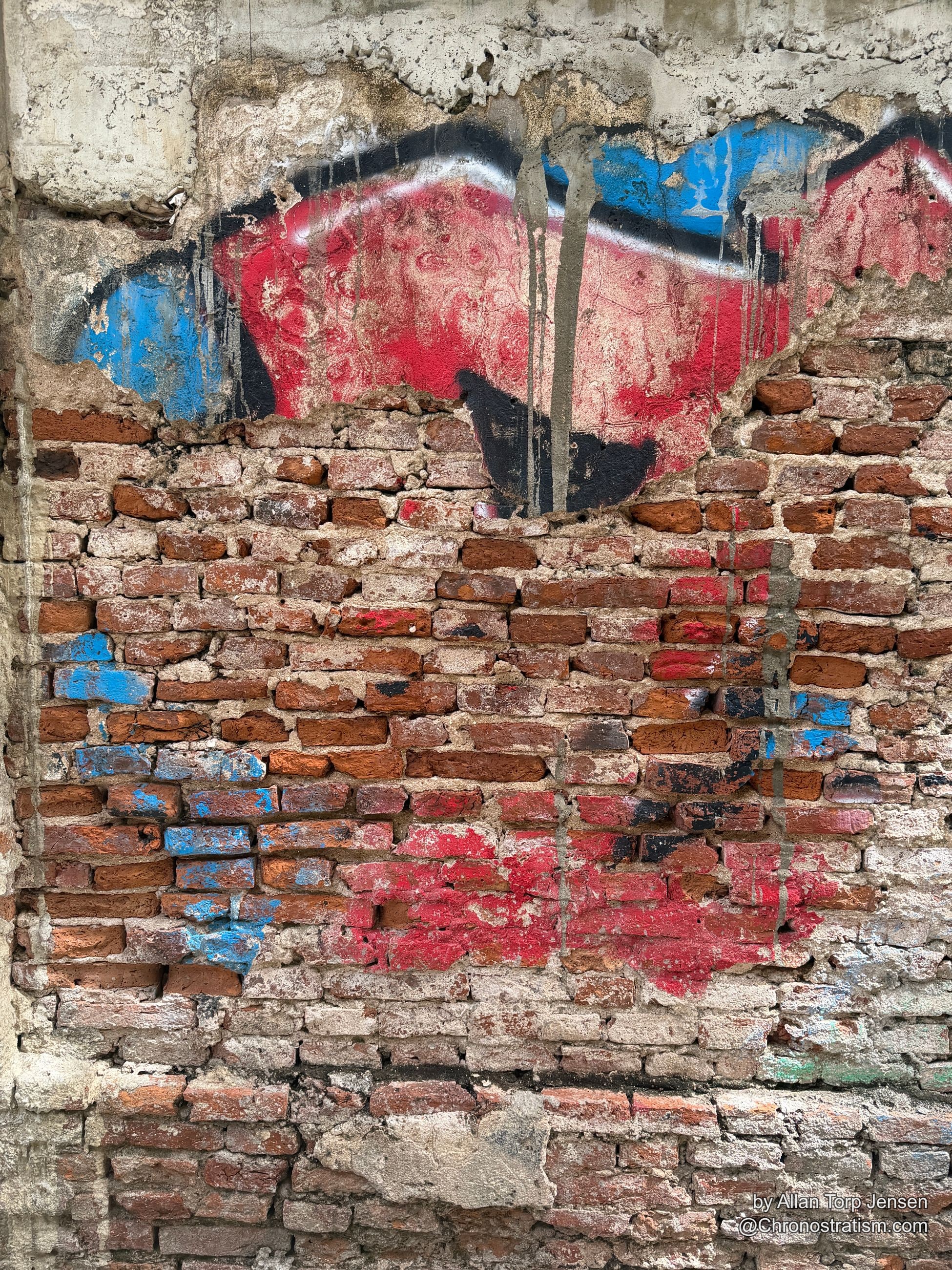 The painted figure’s black silhouette bleeds into blue drips over crumbling brick.