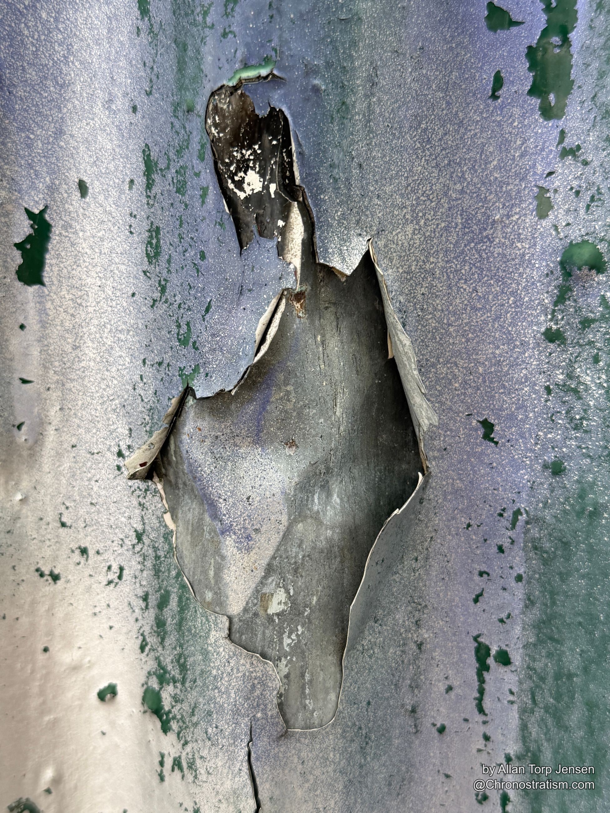 Peeling silver-grey paint tears back in a jagged sheet, dark metal exposed beneath.