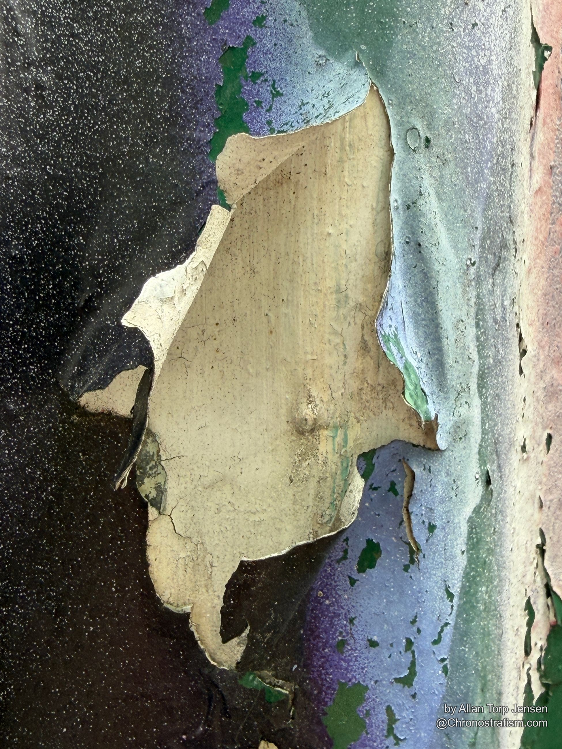 A ragged hole in flaking pale paint reveals cream-coloured metal, cracks radiating outward.