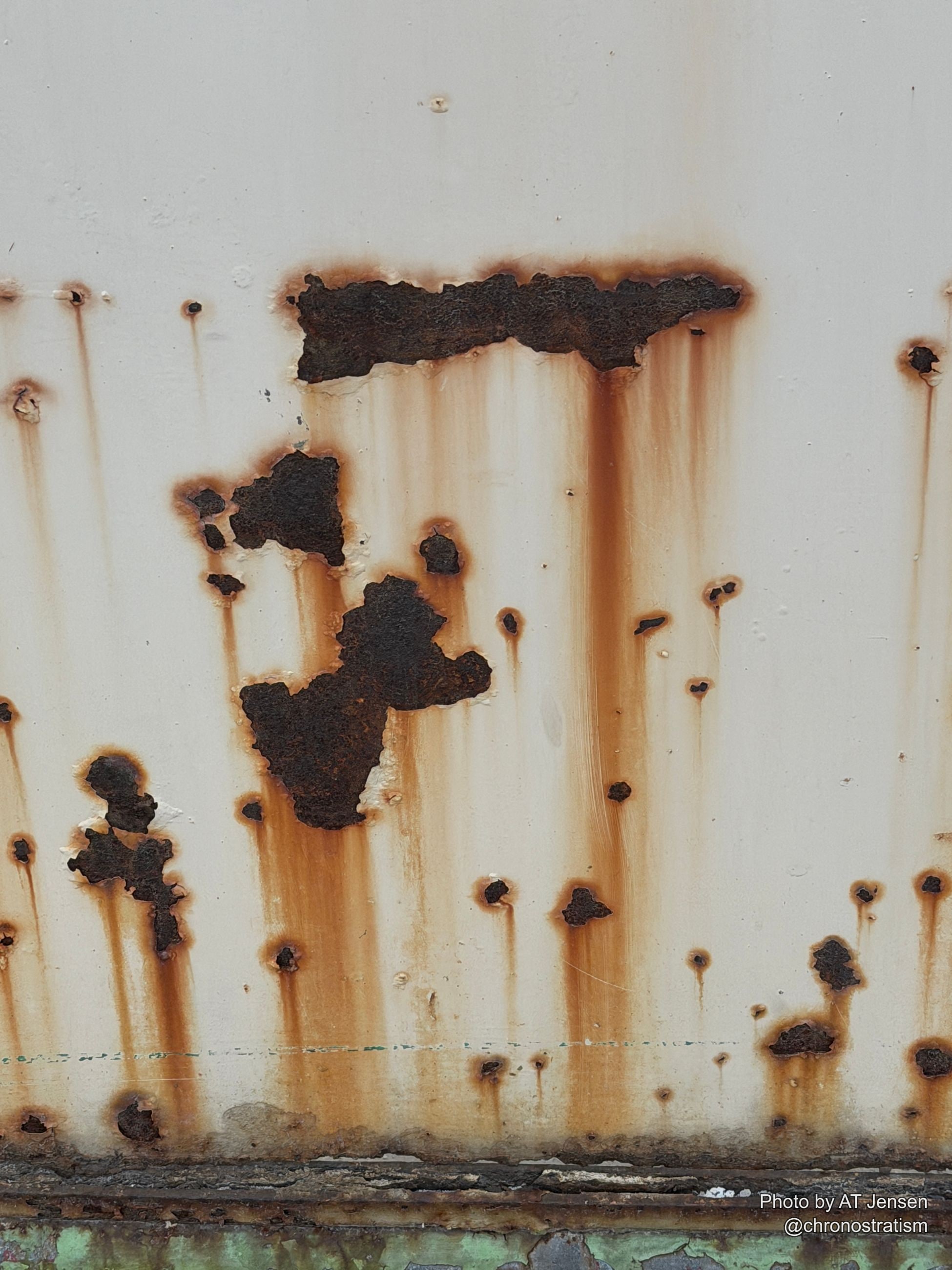 Rust bleeds in streaks down a white panel, perforating through in places.