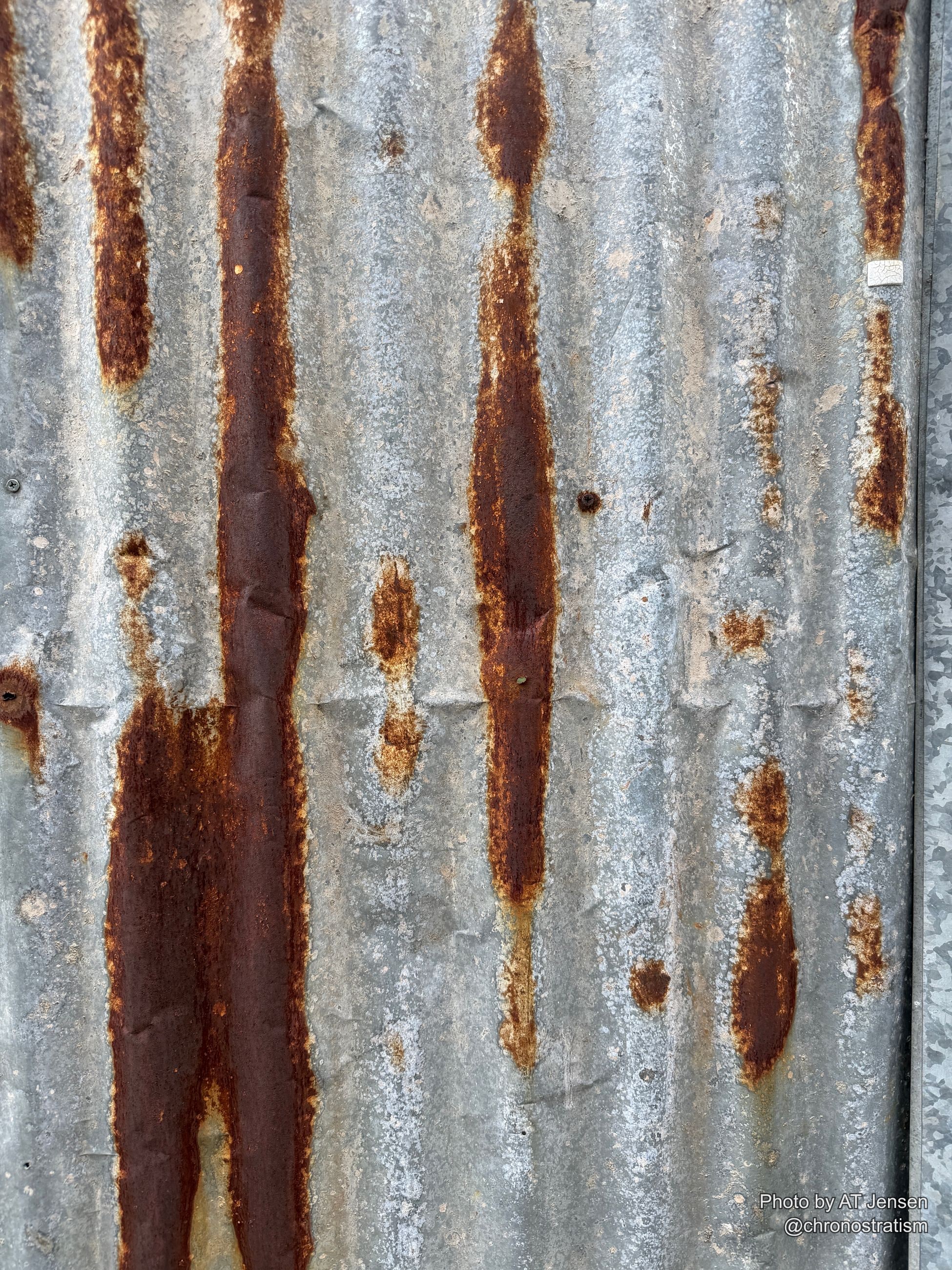 Rust patches spread across a galvanized panel beneath a torn paper sticker.
