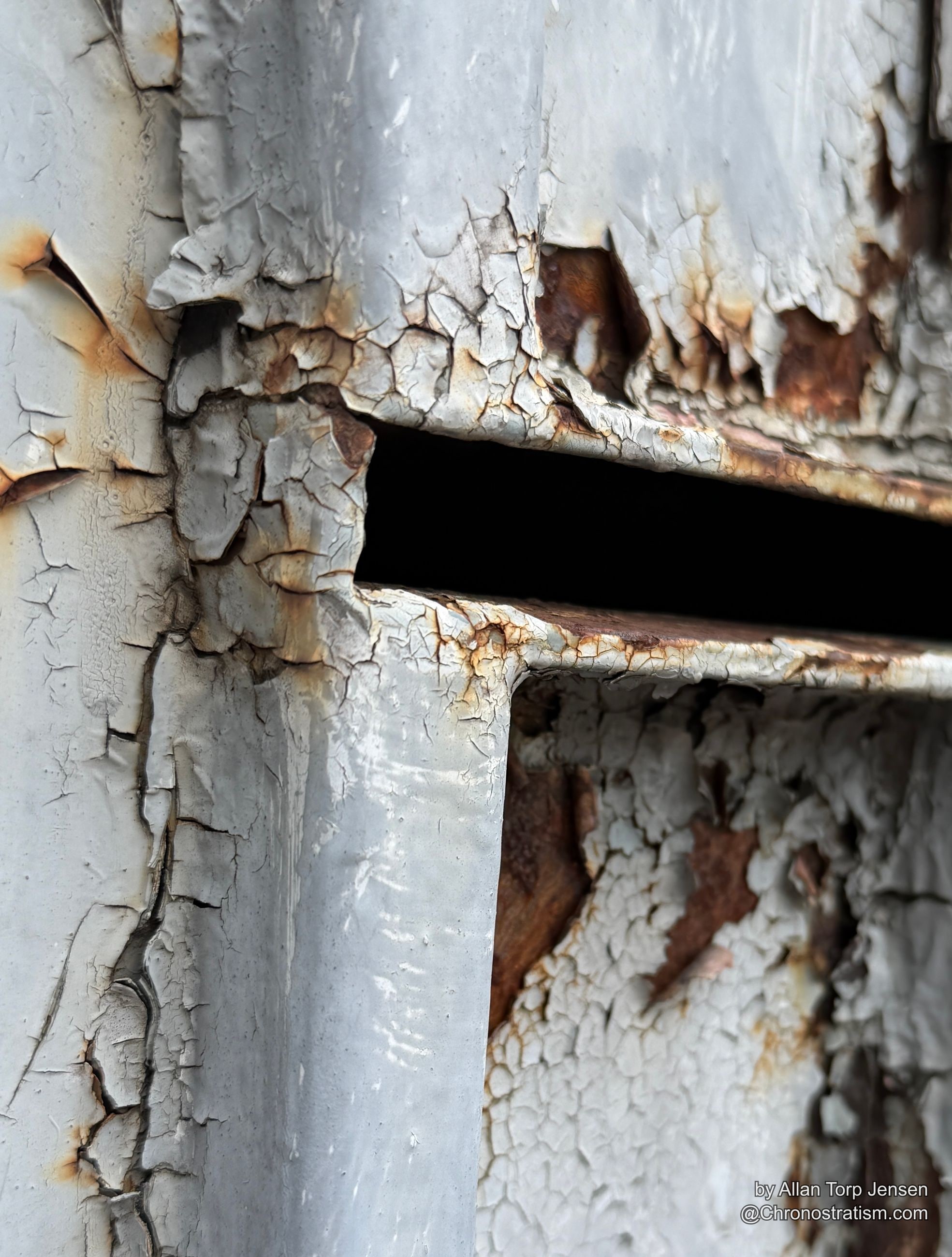 Rust streaks bleed from beneath a mail slot’s peeling paint in tight cracked patterns.