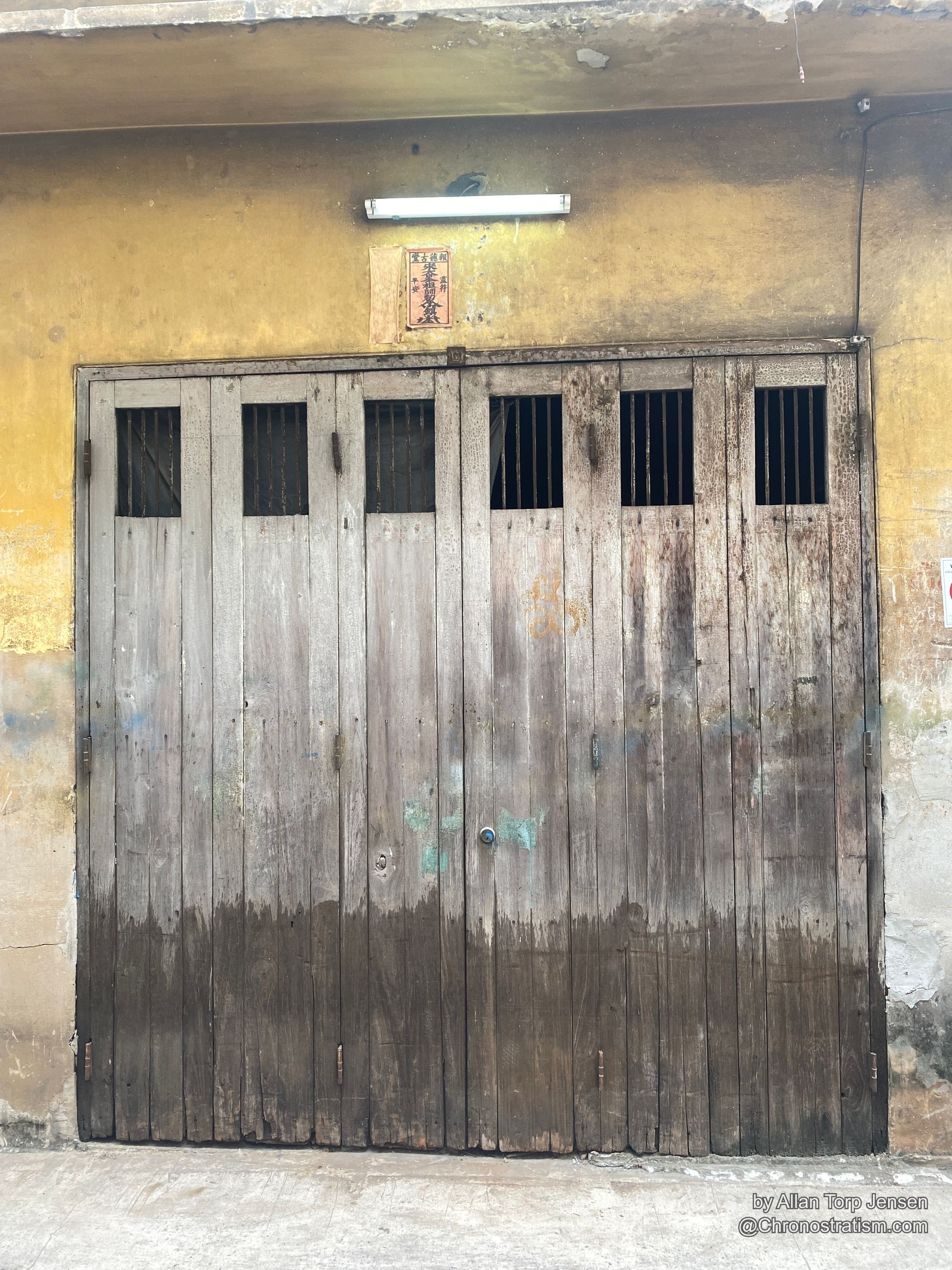 A slatted timber shutter door, one half darkened by water staining, teal paint fleck at centre.