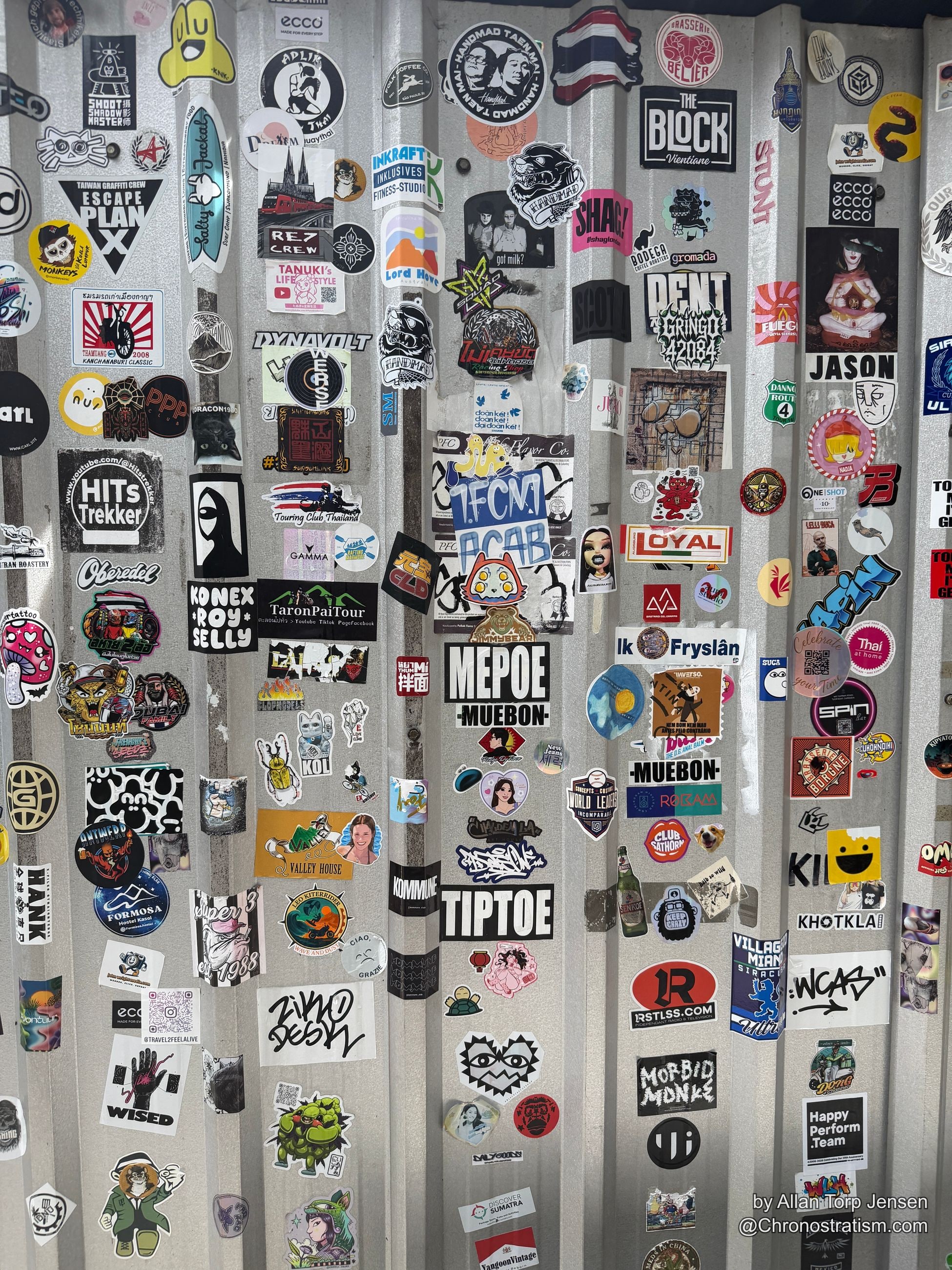 Stickers and crew tags cover a ridged corrugated metal surface.