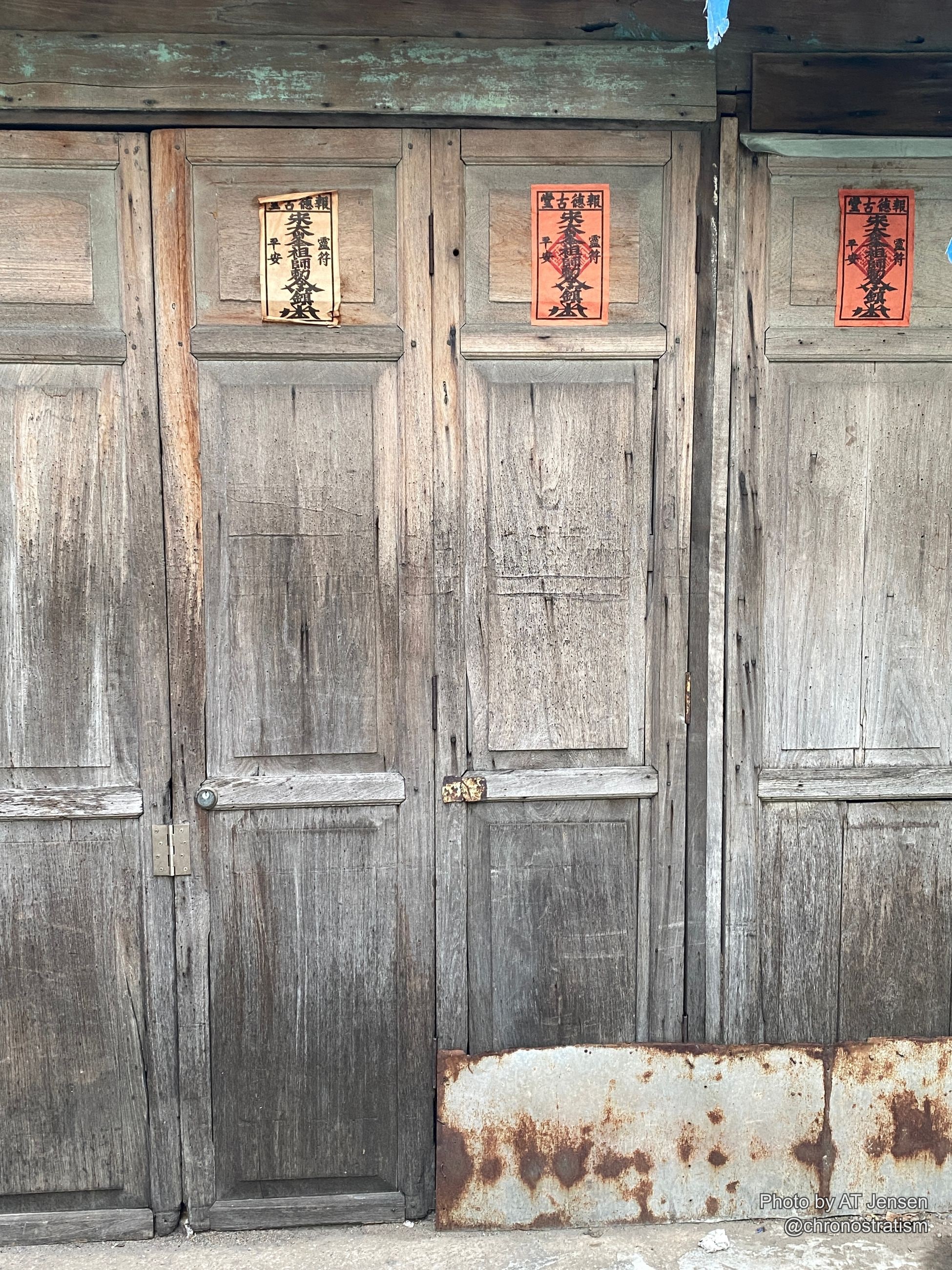 Three printed talisman papers repeat down a row of weathered carved door panels.