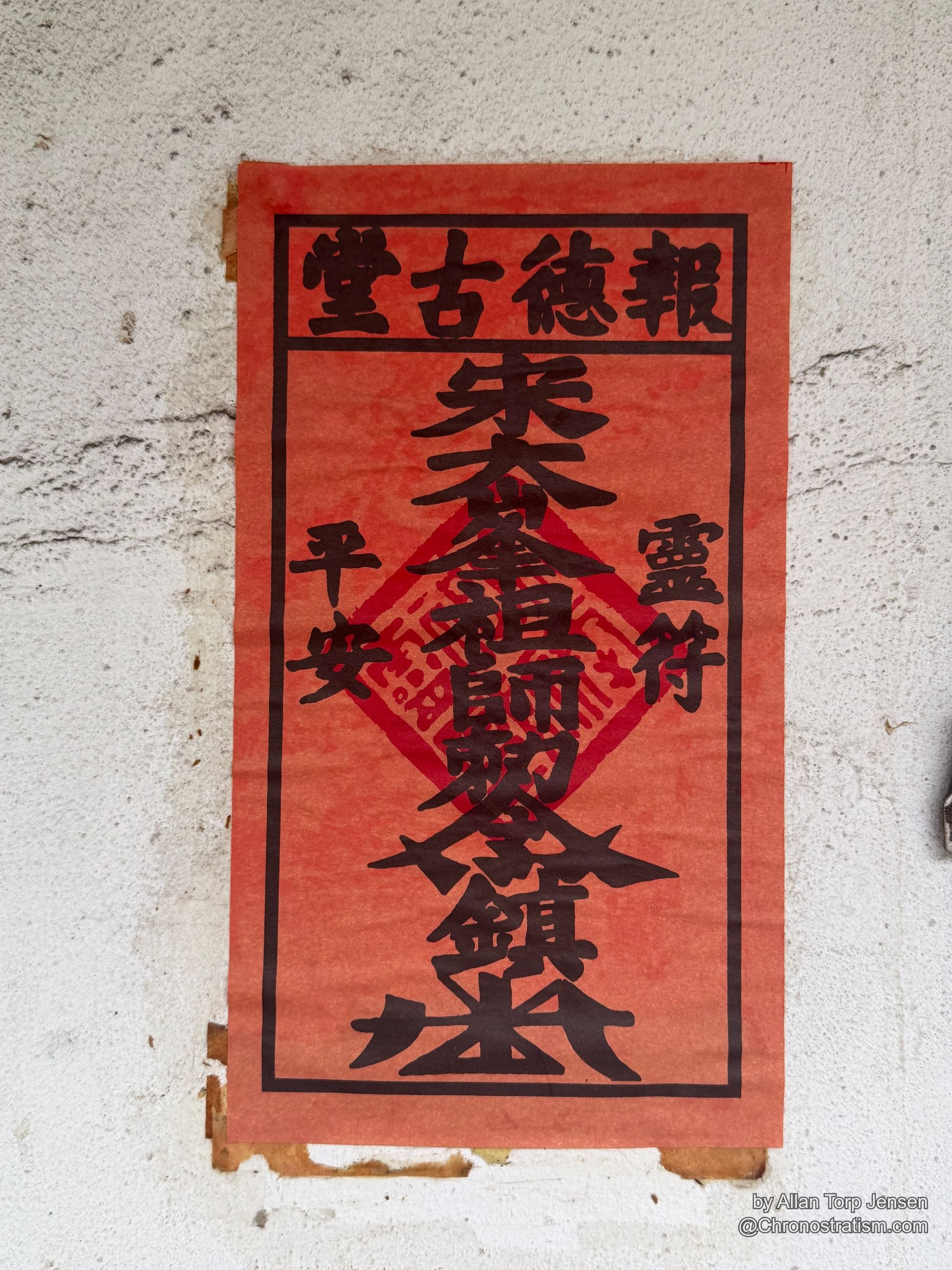 A torn red ritual paper with Chinese characters clings to a weathered white stucco wall.