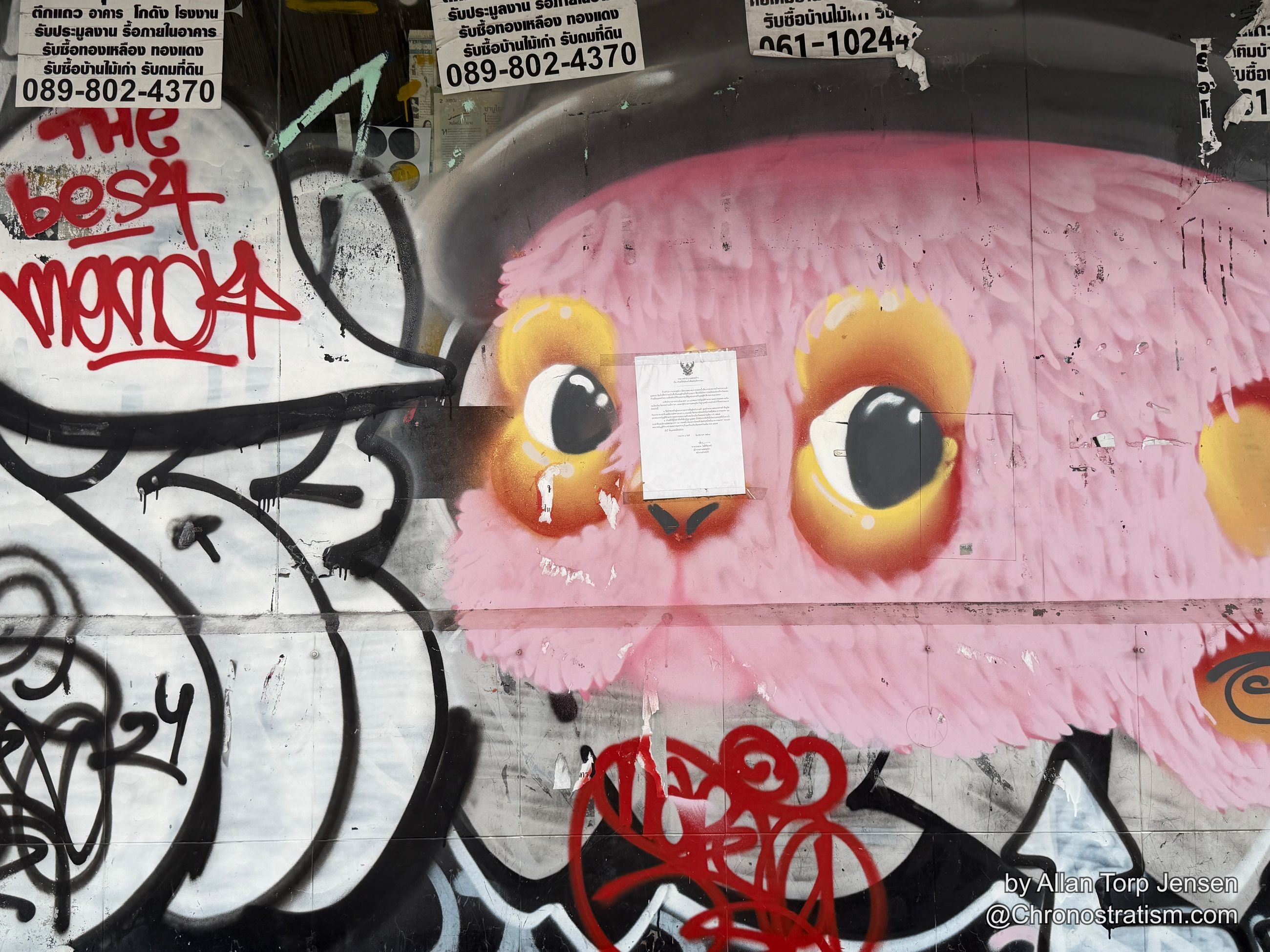 A vivid pink character mural with cartoon eyes shares a wall with red tag lettering and business stickers.