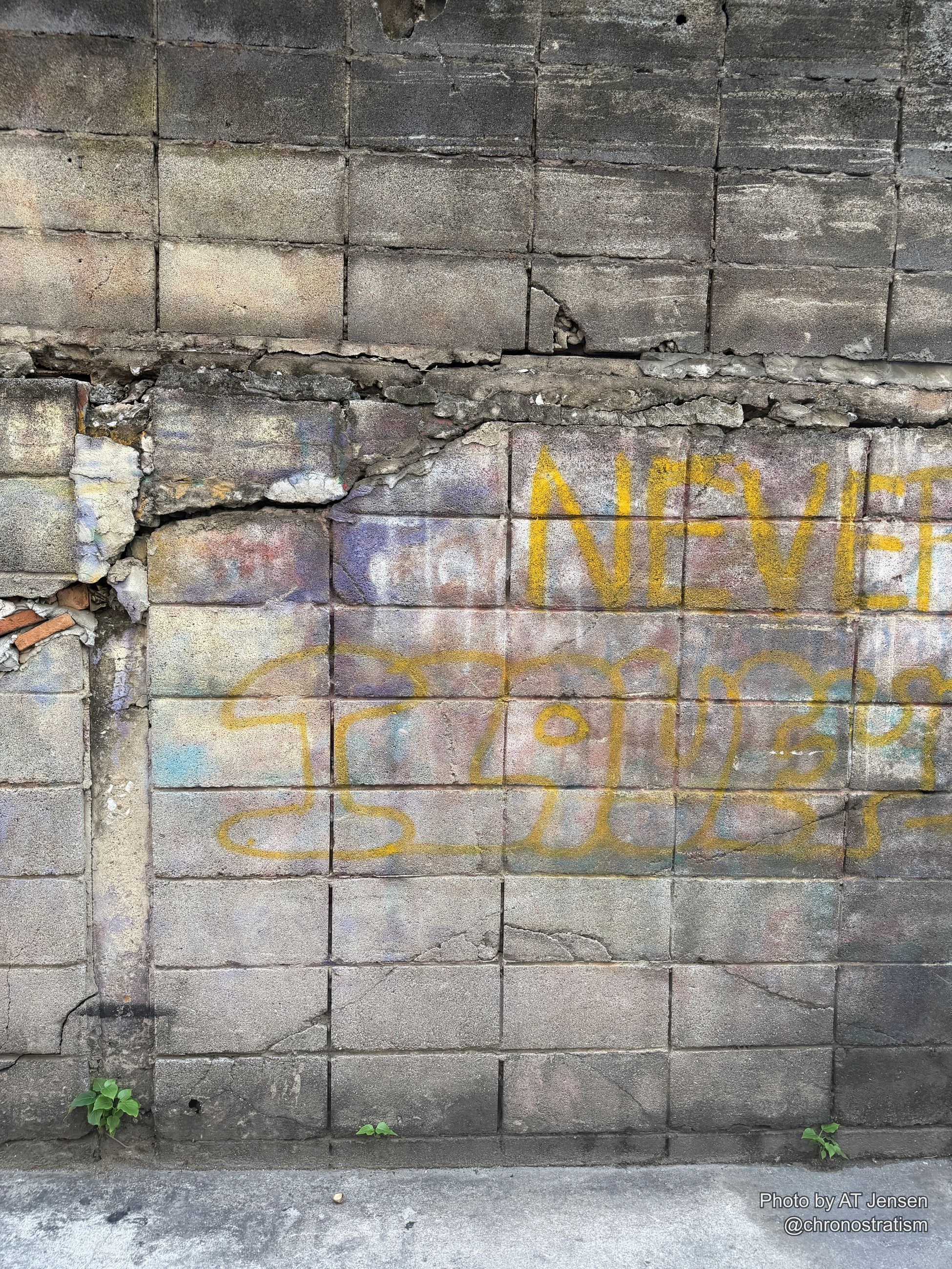 Vivid yellow spray-paint graffiti letters sprawl across a cracked tiled wall.