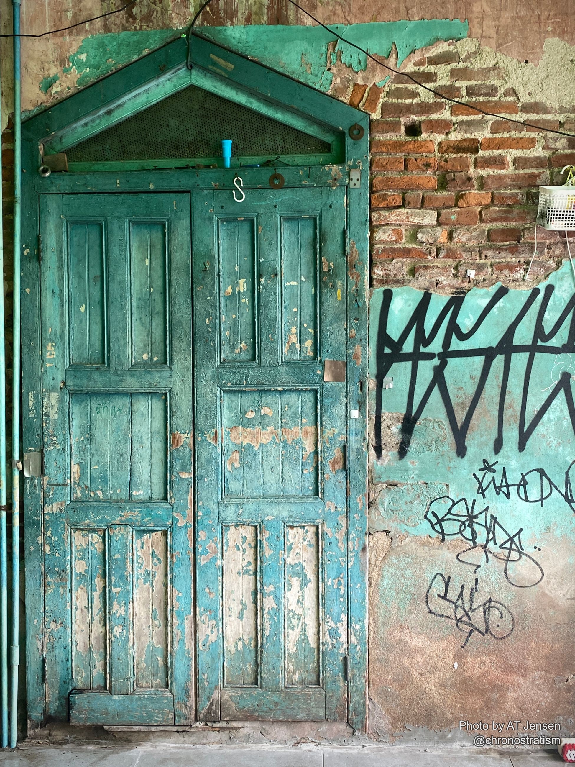 Weathered teal double doors peel in dramatic layers beside a graffiti-tagged brick wall.