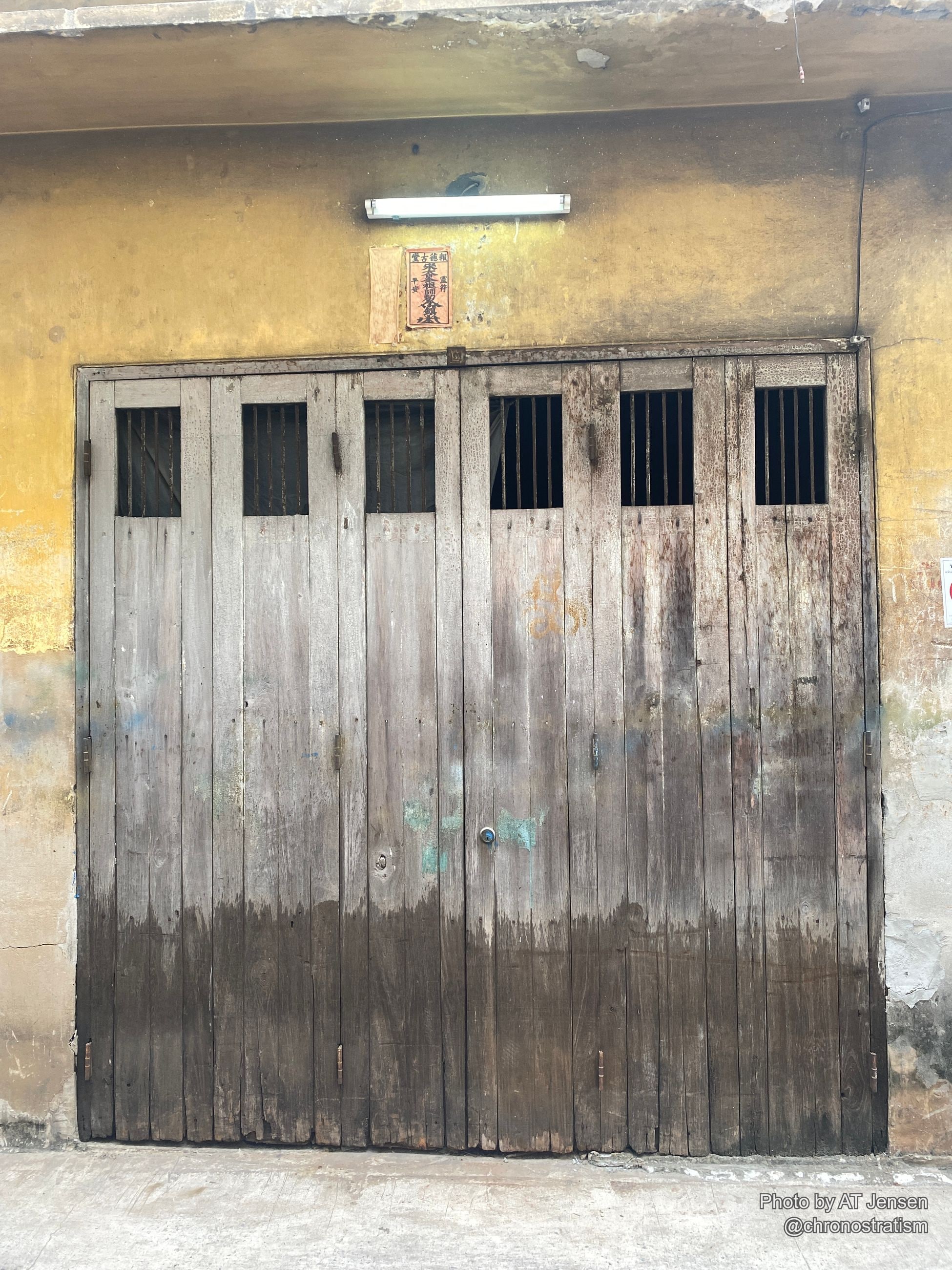 A weathered wooden shutter splits sharply between dark stain and faded grey wood.