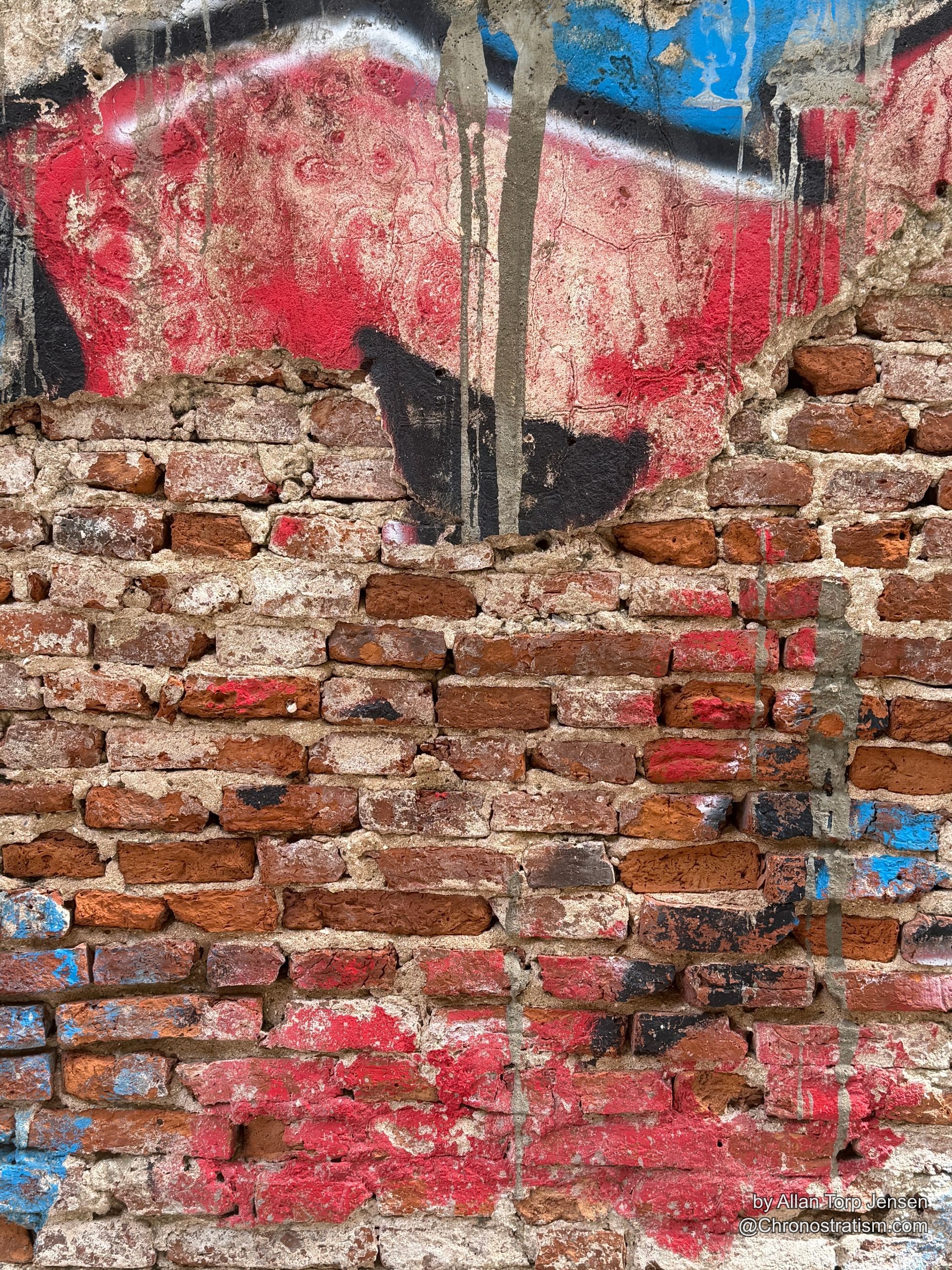 Wide view of the painted brick wall — a red and black shape over patched, multicoloured brickwork.