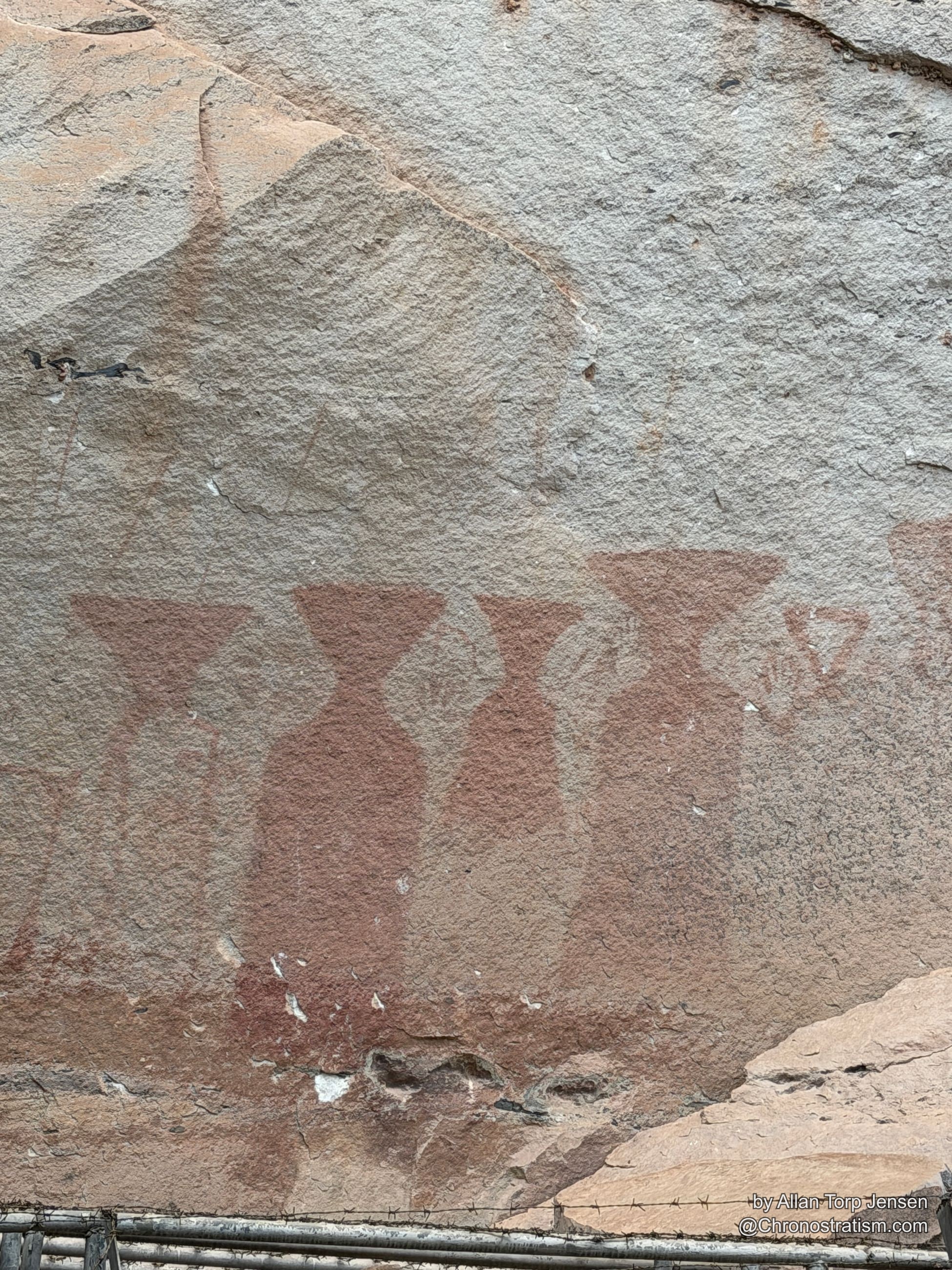 Wide view of the pictograph wall with barbed wire fencing crossing the frame.